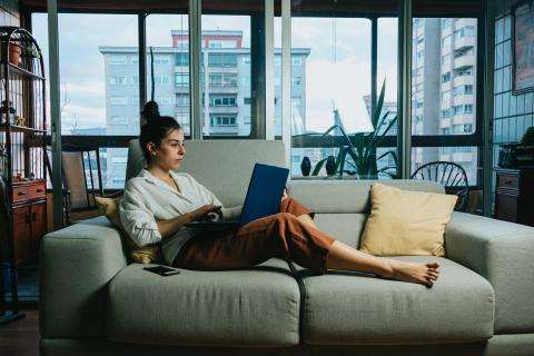 En kvinde sidder med sin computer på en sofa